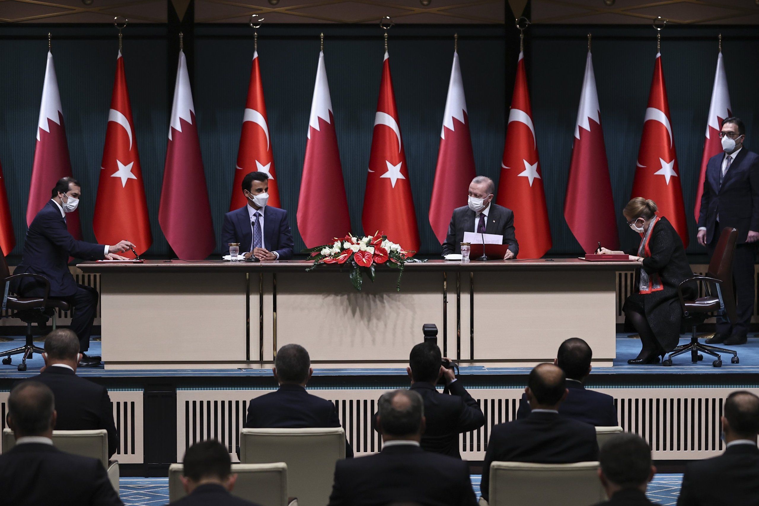 Members from Turkish and Qatari government at a press conference, signing trade documents in front of country flags 