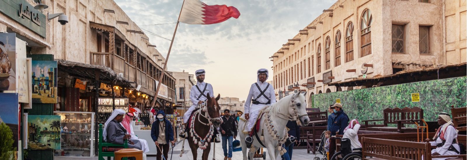 Men in traditional clothing, riding horses in the middle of a busy market street