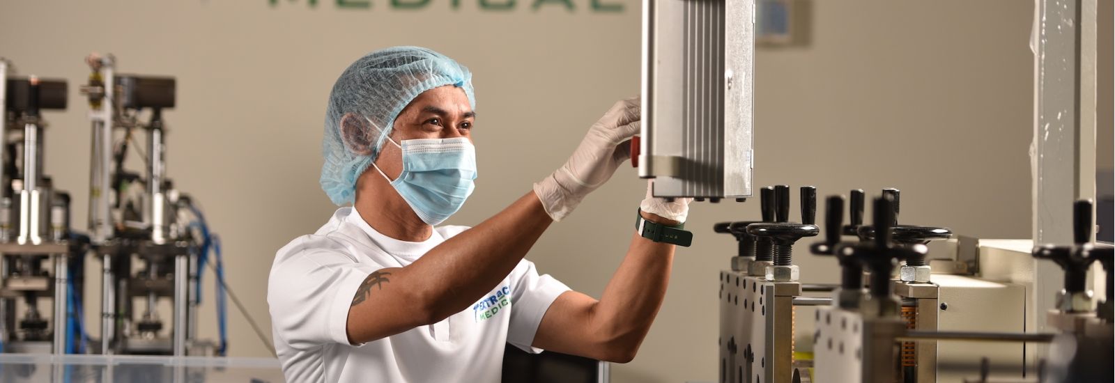 Man in hairnet and mask working on manufacturing equipment