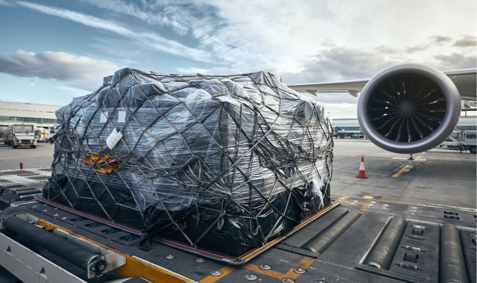 Large amount of air cargo, neatly packaged sitting on a runway, with airplane in background